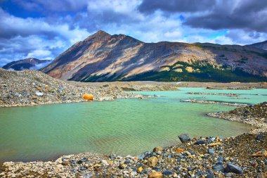 Athabasca Buzul Gölü 'nün turkuaz suları bu ikonik manzaranın vahşi güzelliğini yansıtan canlı gökyüzünün altında kayalık moraine ve Jasper Kanada' da dramatik bir dağ zirvesini yansıtır..