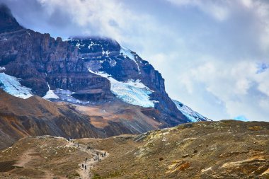 Yürüyüşçüler Jasper Ulusal Parkı 'ndaki Athabasca Buzulu' na doğru engebeli bir yolda ilerliyorlar. Kanada 'da dramatik dağlar ve bulutlar ilham verici bir açık hava macera sahnesi yaratıyor..