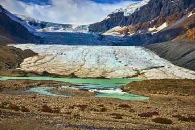 Jasper Kanada 'daki Athabasca Buzulu, buzlu engebeli dağ zeminiyle ve ön plandaki çarpıcı turkuaz eriyen su havuzlarıyla manzaraya hakim..