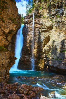 Manzaralı bir şelale, Johnston Canyon Banff Kanada 'da engebeli kayalar ve yemyeşil ağaçlarla çevrili kristal mavi bir havuza düşer..