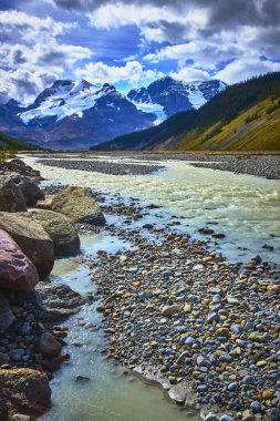 Athabasca Buzulu 'ndan akan bir nehir heybetli kar tepeli dağların çerçevelediği kayalık bir vadiden akıyor Jasper Kanada' da dramatik bir gökyüzünün altında..