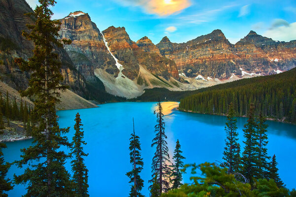 Sunrise at Lake Moraine in Banff Canada bathes turquoise water pine trees and towering mountains in golden hour light creating a serene and inspiring natural landscape.