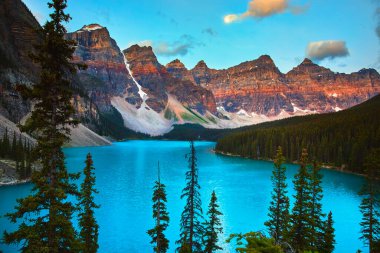 Canlı gündoğumu Moraines Gölü turkuvaz suyunu aydınlatıyor. Banff Canada 'da yeşil orman ve görkemli Rocky Dağları ile çevrili. Altın saat sükuneti ve doğal güzelliği yakalıyor..