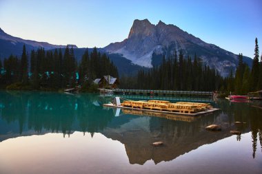 Yoho 'daki Zümrüt Gölü' nün sakin suları, yüksek dağları, tahta bir köprüyü ve alacakaranlıkta yemyeşil bir ormanı yansıtır. Bu da doğadan kaçmak ve rahatlamak için mükemmel bir ortam yaratır..