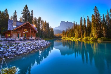 Güneş doğarken Zümrüt Gölü 'nde altın bir parıltı saçar. Yoho Kanada' da berrak bir gökyüzünün altında uzak dağlar tarafından çerçevelenmiş çam ormanlarının ve kır sularının yansımaları..