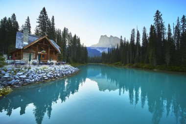 Yoho Kanada 'da güneşin doğuşunda yüksek çam ve dağ manzaralarıyla çevrili Emerald Gölü' nün turkuaz sularının yanında sakin bir altın saat atmosferi oluşturan bir kır evi bulunur..