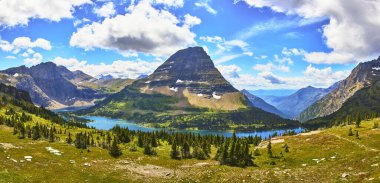 Saklı Göl 'ün geniş bir manzarası ve Montana Buzulu' ndaki Saklı Göl Patikası boyunca canlı bir gökyüzü altında Alp çayır ve orman tarafından çerçevelenmiş dramatik bir dağ zirvesi..
