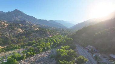 Üç Nehir 'deki Kaweah Nehri' nin üzerinden uçan hava uçuşu canlı yeşil ağaçlar dağ yolunu ve günışığı zirvelerini sararak huzurlu havayı ve ileri doğru hareketliliği yakalıyor..