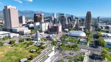 Utah Salt Lake City üzerinde uçan hava aracı Tapınak Meydanı 'nı ve dağ manzaralı şehir siluetini gözler önüne seriyor. Güneşli sokaklar ve bereketli peyzaj bu şehirde davetkar bir şehir atmosferi yaratır.