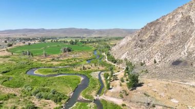 Cokeville Wyoming 'deki dolambaçlı nehir vadisinde uçan hava uçuşu engebeli yamaçlar ve Lejyon Parkı' nı aydınlatıyor. Kamera, nehri takip ederek yeşil tarlaları geçiyor.