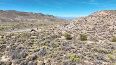 Palmetto California 'daki tarihi taş kalıntılarının üzerinden uçan hava aracı Beyaz Dağ çöl manzarasını ve yol kenarını gösteriyor. Güneş ışığı engebeli araziyi ve uzak hissi vurgular