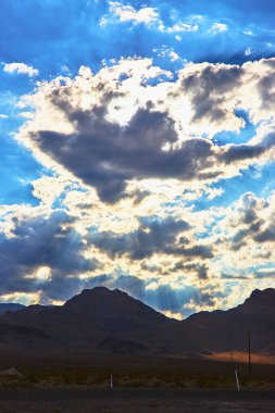 Güneş ışınları Nevada 'daki Charleston Dağı' nın siluetinin üzerindeki dramatik bulutları delip geçer. Uçsuz bucaksız çöl manzarası ve çarpıcı ışık Las Vegas yakınlarında büyüleyici bir manzara yaratır..