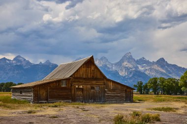 Tarihi TA Moulton Barn Wyoming 'deki Mormon Row' da duruyor. Arka planda dramatik Grand Teton dağları yükseliyor. Huysuz bir gökyüzünün altında klasik bir Amerikan Batı sahnesi yaratıyor..