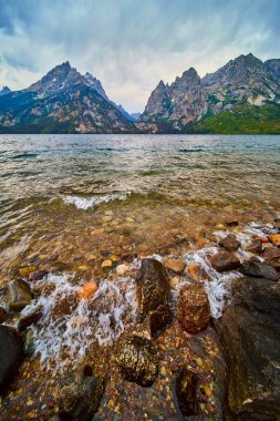 Jenny Gölü 'nün renkli kayalık kıyılarına uzanan berrak su turları Grand Teton dağları Amerika Birleşik Devletleri' nin Wyoming şehrinde kasvetli bir gökyüzünün altında dramatik bir şekilde yükseliyor..