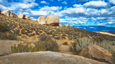 Kaliforniya 'daki Buttermilk Kayaları' nın engebeli yamacına çarpıcı bir gökyüzü altında büyük kayalar hükmediyor. Çöl çalıları ve uzak dağlar bu Doğu Sierra manzarasına derinlik ve doğal güzellik katıyor.