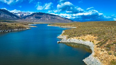 Crowley Gölü 'nün engebeli kıyı şeridi ve karla kaplı dağlarıyla Doğu Sierra' da Bishop California yakınlarında. Parlak mavi su ve dramatik bulutlar çarpıcı bir doğal manzara yaratır..
