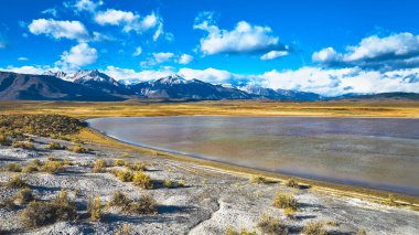 Kaliforniya 'daki Owens Vadisi boyunca uzanan sakin bir göl karla kaplı dağlar ve parlak bir gökyüzünün altındaki açık arazilerle çevrili. Güneşli bulutlar ve engebeli arazi çarpıcı bir Doğu Sierra yaratıyor.