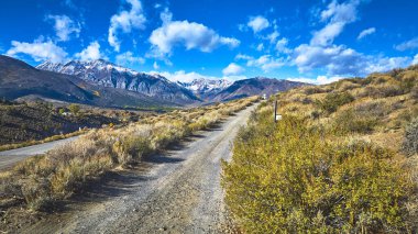 Kuru çalılıklardan geçip California 'nın doğu Sierra bölgesindeki karlı dağlara giden dolambaçlı bir yol var. Parlak mavi gökyüzü ve dramatik bulutlar Crowley Gölü ve Bishop yakınlarındaki manzarayı güzelleştirir..