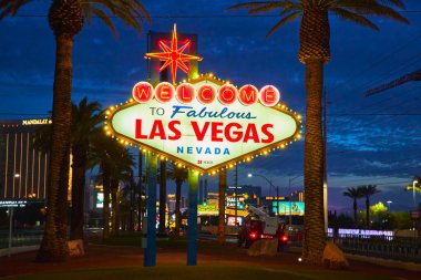 Meşhur Las Vegas Nevada 'ya hoş geldiniz tabelası alacakaranlıkta parlıyor. Palmiye ağaçları ve canlı şeritlerle çerçevelenmiş. Şehir merkezindeki canlı atmosfer Nevada 'daki Las Vegas' ın ruhunu yansıtıyor..