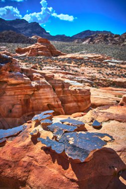 Güneş ışığı, Nevada Çölü 'nde Çamurlu Dağ' ın yakınındaki katmanlı kırmızı kumtaşını ve kil taşını aydınlatır. Engebeli arazi ve uzak tepeler Moapa Vadisi ve Saklı Vadi 'nin kalbinde dramatik bir sahne yaratıyor..