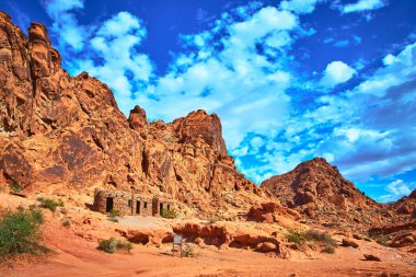 Nevada 'nın Ateş Vadisi' ndeki Kulübe 'nin üzerinden yükselen kızıl kumtaşı kayalıkları gökyüzünü dolduruyor. Moapa Vadisi yakınlarındaki dramatik çöl manzarası doğal güzelliği ve bölgesel tarihi vurguluyor..