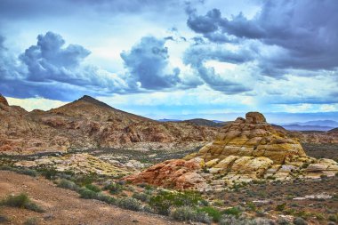 Nevada 'daki Muddy Dağı boyunca canlı kumtaşı oluşumları ve engebeli çöl manzaraları. Moapa Vadisi 'nde ve Bitter Springs Patikası' nda dramatik bulutlar toplanıyor ve güçlü bir doğal manzara yaratıyor..