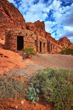 Kulübe Nevada, Ateş Vadisi 'ndeki dramatik kırmızı kumtaşı kayalıklarına karşı duruyor. Güneş ışığı, kır taşlarını, çöl bitkilerini ve çarpan gökyüzünü vurguluyor. Moapa Vadisi 'nin özünü yakalıyor.