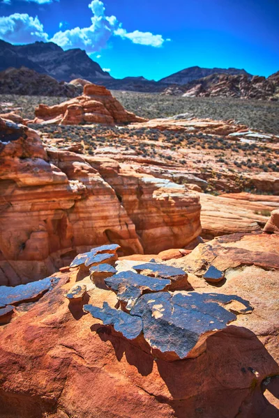 Güneş ışığı, Nevada Çölü 'nde Çamurlu Dağ' ın yakınındaki katmanlı kırmızı kumtaşını ve kil taşını aydınlatır. Engebeli arazi ve uzak tepeler Moapa Vadisi ve Saklı Vadi 'nin kalbinde dramatik bir sahne yaratıyor..