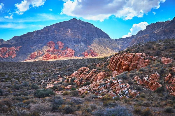 Nevada 'daki Muddy Mountain' ın altında canlı kırmızı kaya oluşumları ve dramatik çöl arazileri bulunuyor. Güneş ışığı, Moapa Vadisi 'nin ve Saklı Vadi' nin dinamik bir gökyüzü altındaki doğal güzelliğini vurgular..