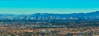 Las Vegas Nevada 'nın hava manzarasında Lone Mountain ile Strip ufuk çizgisi ve açık mavi gökyüzü altında yayılan yerleşim yerleri var. Sahne şehir enerjisini doğal çöl ile harmanlıyor.