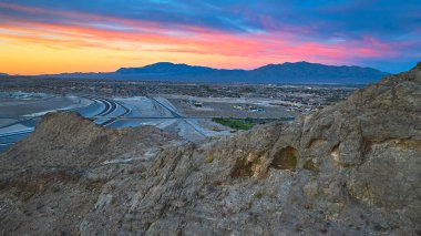 Nevada 'daki Lone Mountain ve Las Vegas' ın dramatik gökyüzü ve çöl arazisiyle altın saat boyunca hava manzarası. Kentsel yayılma, otoyollar ve engebeli dağlar canlı bir güneybatı manzarası yaratır..