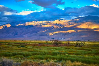 Sabah güneşi, Piskopos California yakınlarındaki Doğu Sierra dağlarını aydınlatıyor. Aşağıdaki vadiyi yeşil otlar dolduruyor ve gökyüzünde dramatik bulutlar sürükleniyor. Bir huzur hissi ve...