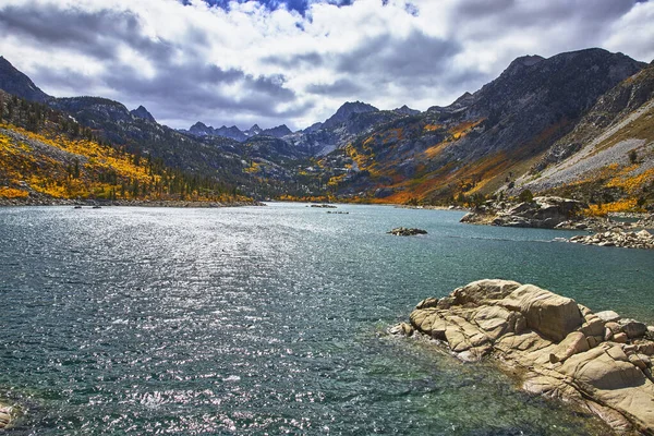 Parlak sonbahar renkleri, Bishop California yakınlarındaki Doğu Sierra 'daki bir dağ gölünün berrak sularını çerçeveler. Dramatik zirveler ve canlı yapraklar dinamik bir ortamda çarpıcı bir mevsimsel atmosfer yaratır.