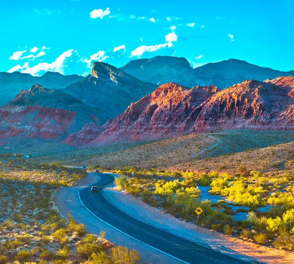 Las Vegas yakınlarındaki Red Rock Kanyonu 'ndan dolambaçlı bir yol geçiyor ve Turtlehead Tepesi uzaklardan yükseliyor. Canlı Nevada çölü ve dramatik dağlar macera hissi yaratıyor.