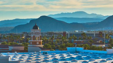 Sıcak altın saat güneş ışığı Las Vegas siluetini yıkıyor. Arka planda Lone Mountain ve Spring Mountain yükseliyor. Palmiye ağaçları ve şehir mimarisi canlı bir çöl manzarası yaratıyor.