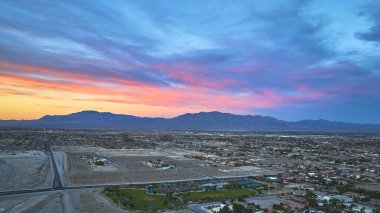 Nevada 'daki Las Vegas' ın hava manzarası, arka planda dağ sıraları ve yukarıda parlak bir altın saat gökyüzü olan çöllerle çevrili genişleyen mahalleleri gözler önüne seriyor. Renkler ve şehir manzarası bir
