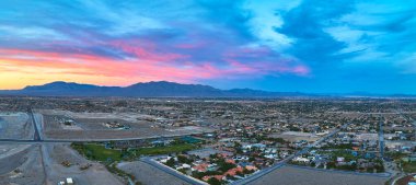 Las Vegas Nevada 'nın havadan görünüşü varoş mahalleleri çöl manzarası ve renkli altın saat gökyüzünün altındaki uzak dağlar. Panorama canlı şehir büyümesini ve doğal manzarasını sergiliyor.
