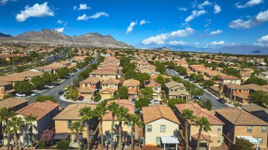Nevada 'da güneşli bir Las Vegas mahallesinin havadan görünüşü modern evlerin sırasıyla yemyeşil ve parlak mavi gökyüzünün altında yükselen dağlar..