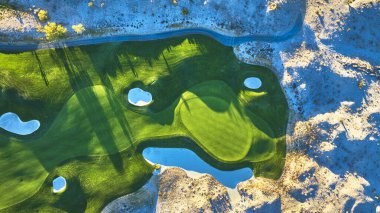 Las Vegas Nevada 'daki bir golf sahasının altın saatinde parlak çöl manzarasının yanında canlı yeşil çayırları gösteren hava manzarası. Karşıt dokular ve zengin ışık bu eşsiz eğlenceyi vurgular