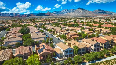 Las Vegas Nevada 'da bir yerleşim bölgesinin havadan görüntüsü. Uzakta Kızıl Kaya dağları ve parlak mavi gökyüzünün altında bol yeşillik. Sahne, banliyö evleri toplumunu yakalıyor ve