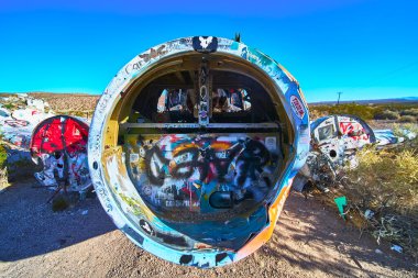 Parçalanmış bir uçak, renkli graffitilerle kaplı Beatty yakınlarında Nevada çölünde oturuyor. Parlak güneş ışığı, kurak araziye ve açık mavi gökyüzüne karşı yaratıcı sokak sanatını ön plana çıkarıyor.