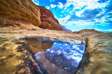 Sakin bir su birikintisi Las Vegas Nevada yakınlarındaki Red Rock Kanyonu 'nun ikonik kumtaşının ortasındaki dramatik gökyüzünü yansıtır. Sahnede bu eşsiz çölde canlı dokular ve doğal güzellikler var.