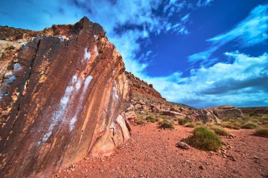 Kızıl Kaya Kanyonu 'nda parlak mavi Nevada gökyüzünün altında belirgin tebeşir izleriyle dramatik bir kum taşı tırmanma duvarı bulunuyor. Engebeli çöl arazisi ve uzak tepeler macera hissi uyandırıyor.