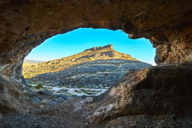 Mağaranın içinden dramatik bir manzara güneşli çöl tepelerine ve engebeli araziye bakıyor. Doğal çerçeve Las Vegas Nevada ve Peekaboo yakınlarında bulunan eşsiz jeolojiyi ve kurak güzelliği vurguluyor.