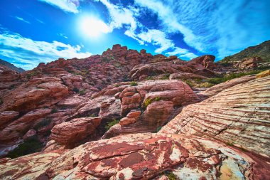 Las Vegas Nevada yakınlarındaki Red Rock Kanyonu 'ndaki katmanlı kumtaşı kayalarının üzerinden geçen güneş ışığı akıntıları tepemizde mavi gökyüzüne çarpıyor. Dramatik çöl manzarası Kraft Dağı ve eşsiz jeolojiyi vurguluyor.