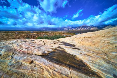 Las Vegas Nevada yakınlarındaki Red Rock Kanyonu 'nun üzerinde renkli Calico kumtaşı yükseliyor. Küçük bir su birikintisi dramatik gökyüzünü ve uzak dağları yansıtıyor. Canlı manzara benzersiz bir manzara sunar.