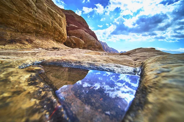 Sakin bir su birikintisi Las Vegas Nevada yakınlarındaki Red Rock Kanyonu 'nun ikonik kumtaşının ortasındaki dramatik gökyüzünü yansıtır. Sahnede bu eşsiz çölde canlı dokular ve doğal güzellikler var.