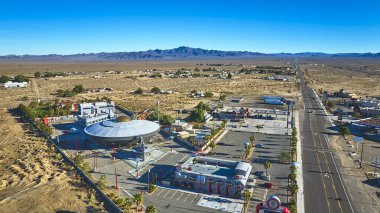 Baker California 'daki ünlü uzaylı temalı çekimin havadan görünüşü geniş bir çöl manzarasına karşı. Açık mavi gökyüzünün ve parlak güneş ışığının altında uzun bir otoyol uzanır..
