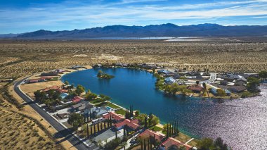 Yermo California 'da evlerle çevrili canlı mavi bir gölet ve berrak bir gökyüzü altında geniş bir çöl ve dağ manzarasına karşı kurulmuş sakin bir mahalle..