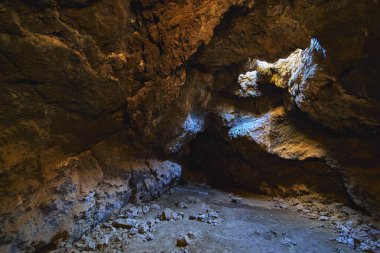 Güneş ışığı Mojave Çölü Kaliforniya 'sındaki Kelso Lava Tüneli' ne akar ve engebeli volkanik kayaları ve dramatik bir mağara içini aydınlatır. Dağıtılmış taşlar ve desenli duvarlar hissi artırır.